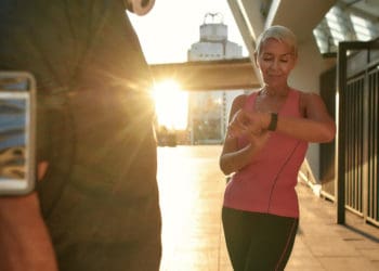 Great results. beautiful and fit middle aged woman in sports clothing looking at smartwatch while training with her husband outdoors