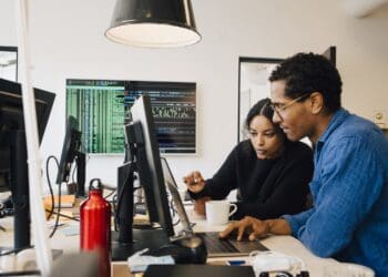 Focused male and female engineers coding over laptop on desk in office